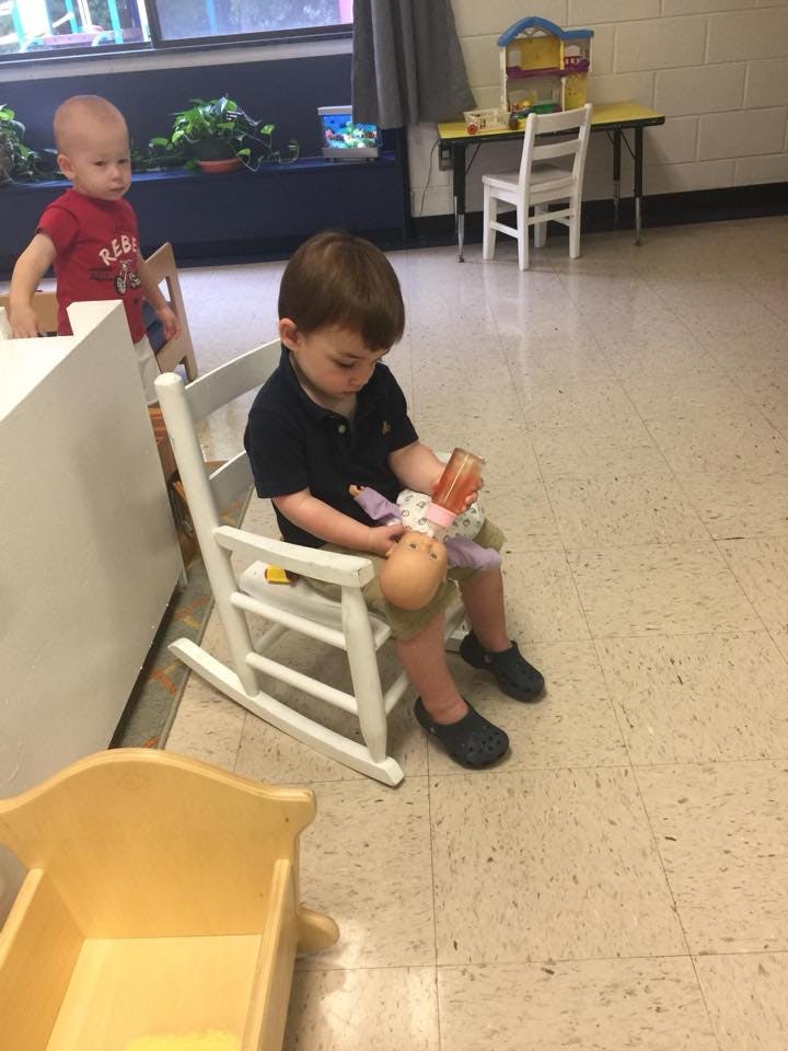 Child sitting in a rocking chair holding a doll and bottle