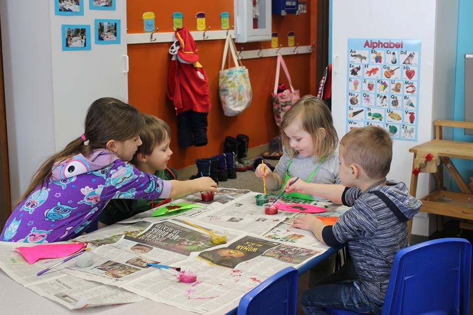 Four children painting at a table in a classroom