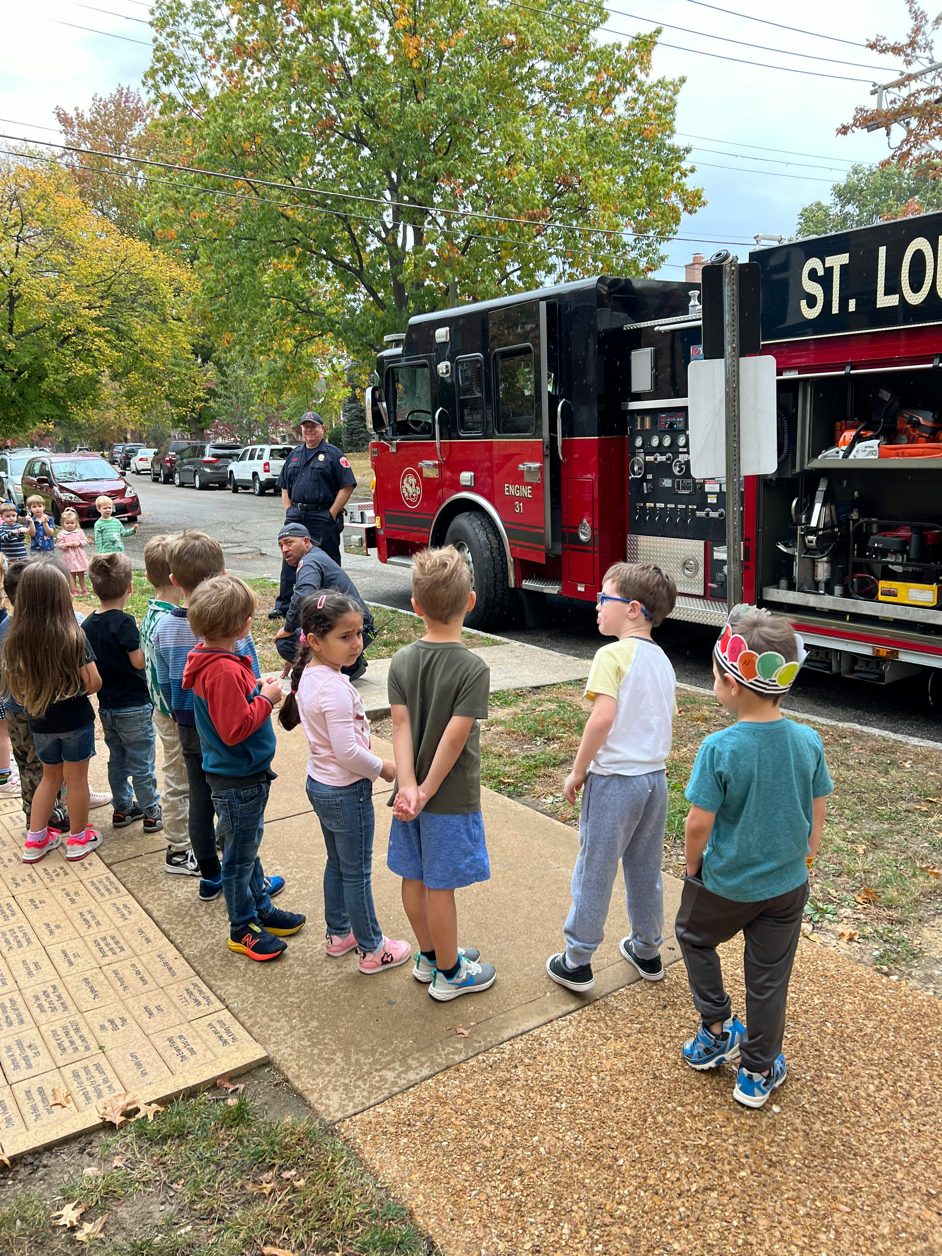 Children standing on a sidewalk looking at a fire truck
