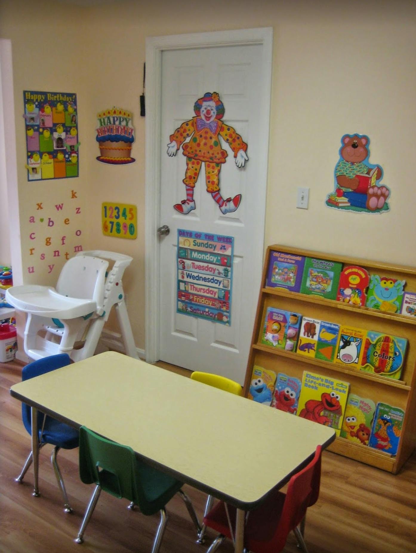 Classroom with a table, chairs, high chair, bookshelf, and wall decorations