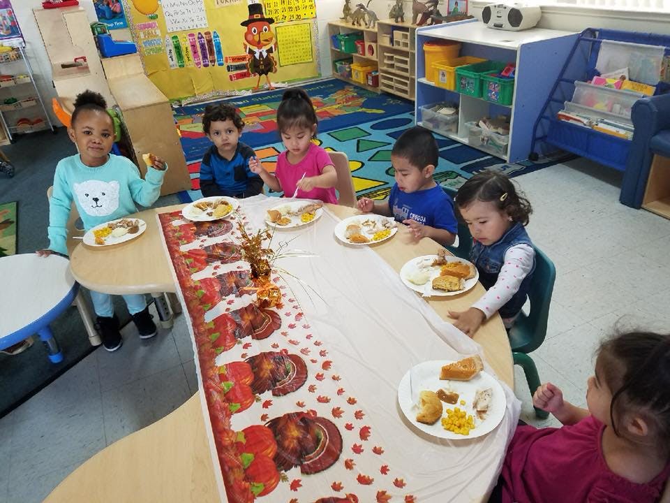 Children sitting at a table with plates of food in a classroom