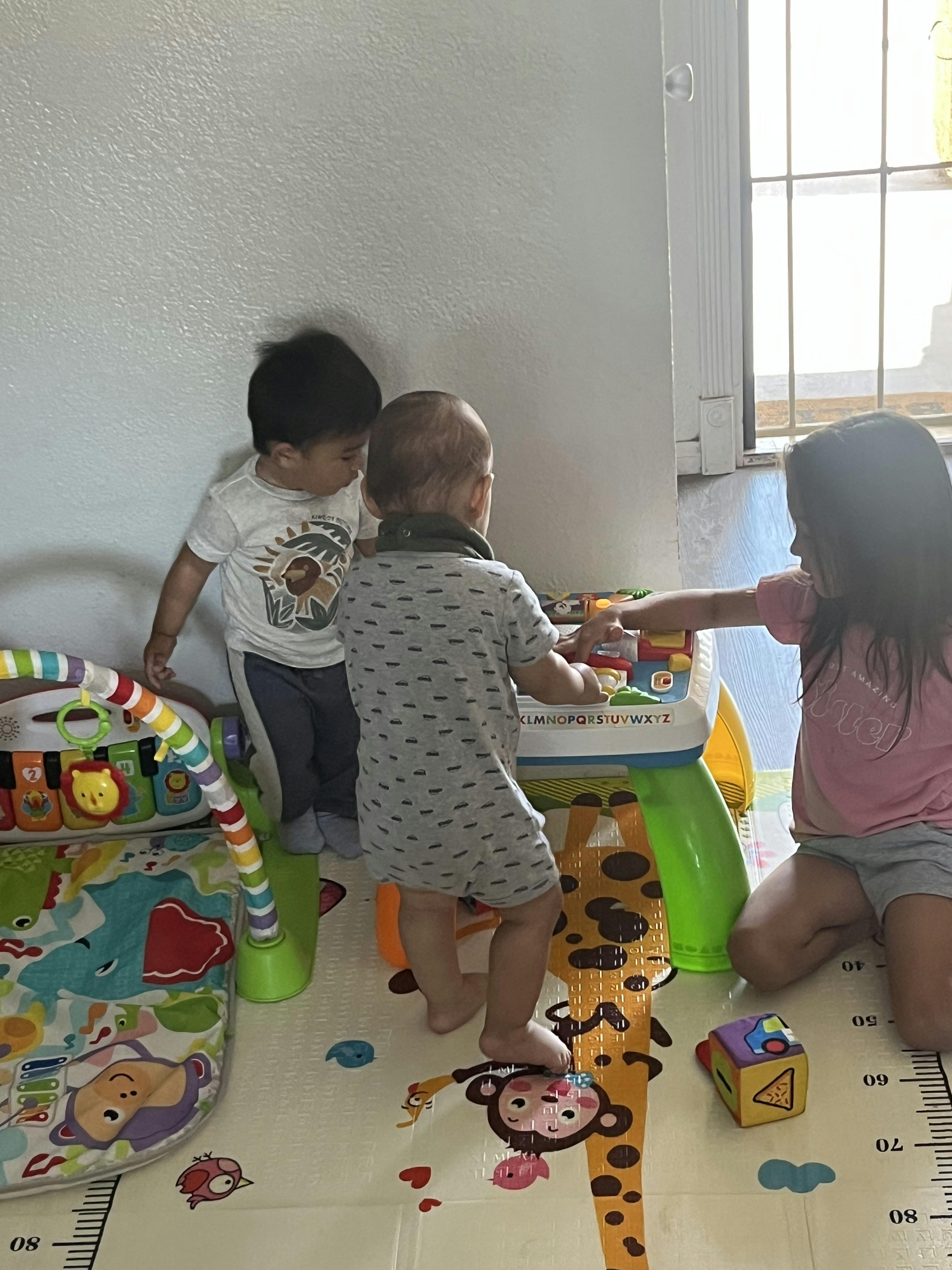 Three children playing with an activity table on a floor mat