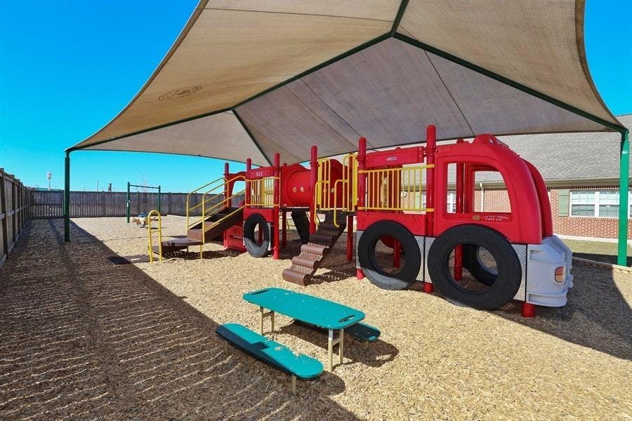 Playground with a red fire truck-shaped play structure under a shade canopy
