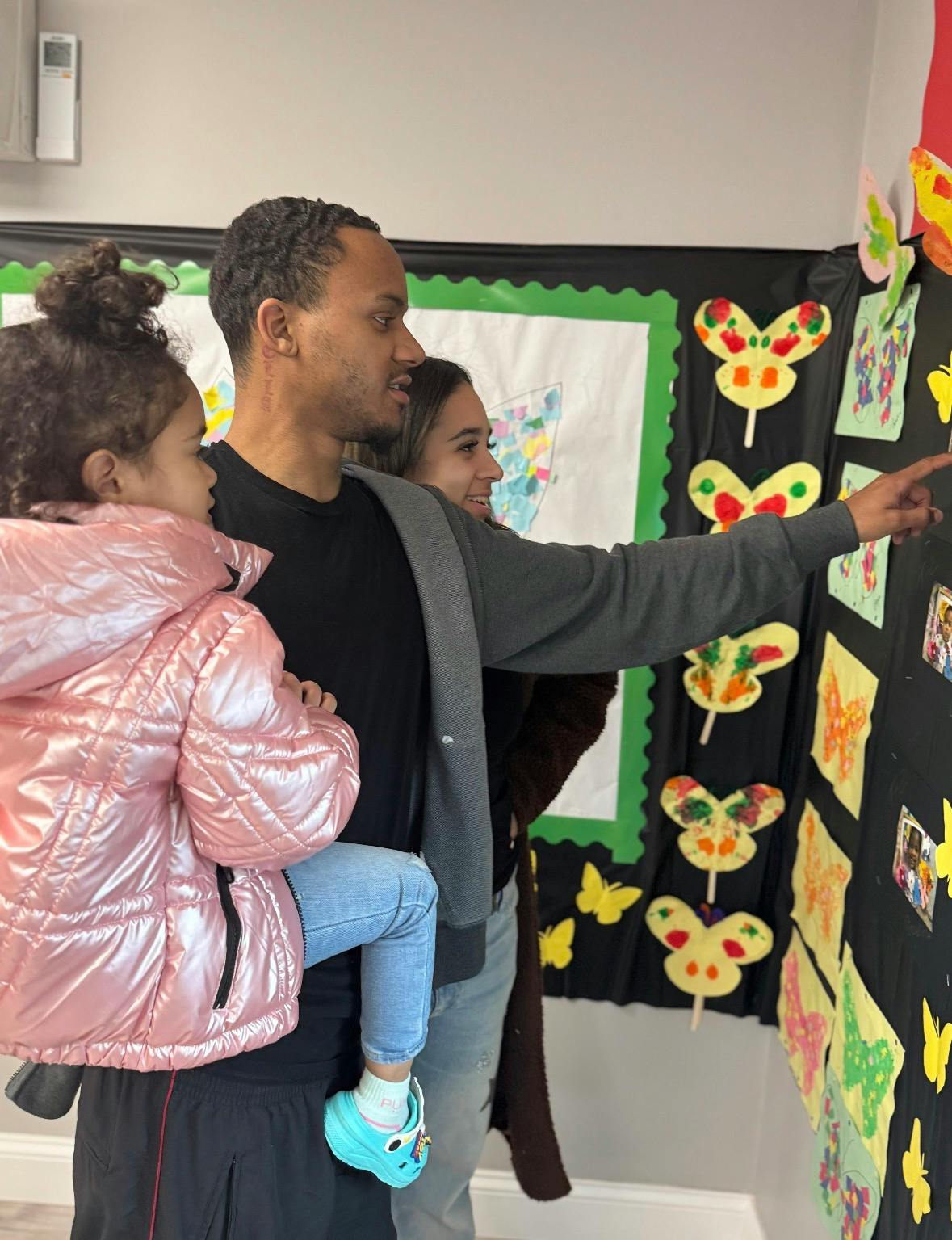 A man holding a child, pointing at a display of butterfly artwork with a woman