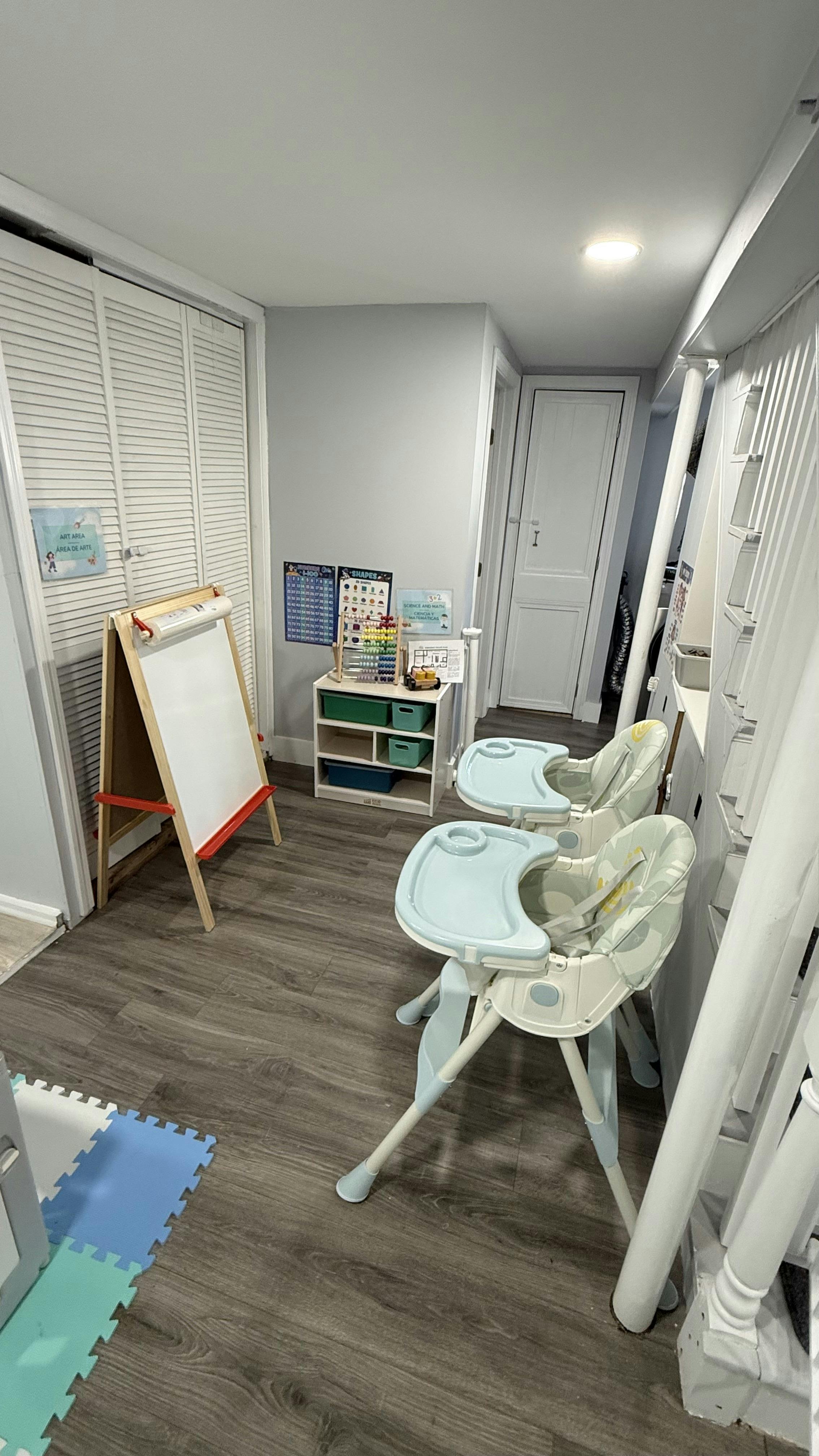 Two high chairs in a room with an easel and storage shelf