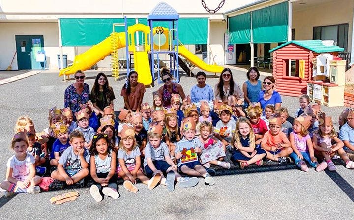 Group of adults and children sitting on the ground in front of a playground