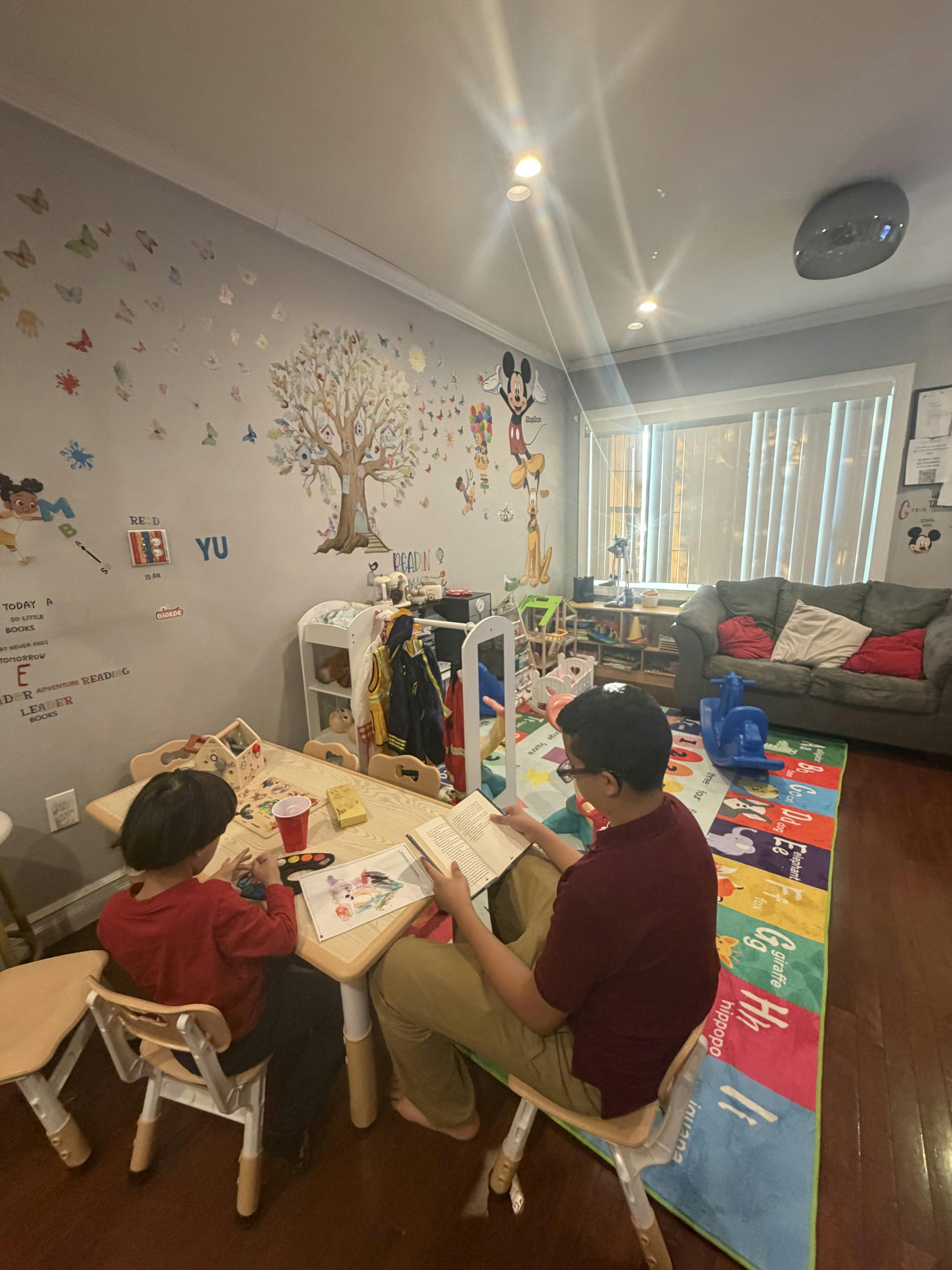 A person reading a book while a child paints at a small table