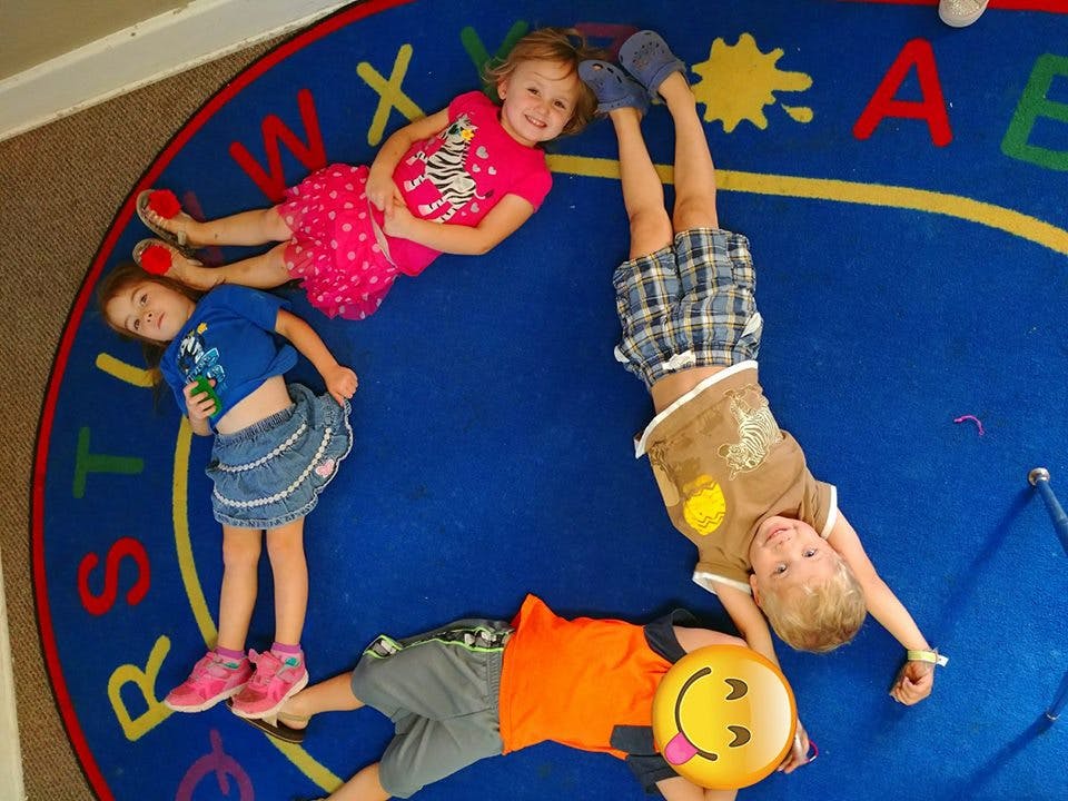Four children lying on a blue alphabet rug