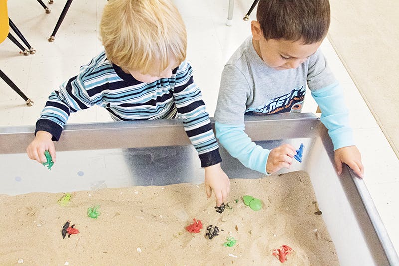 Two children playing with toys in a sand table