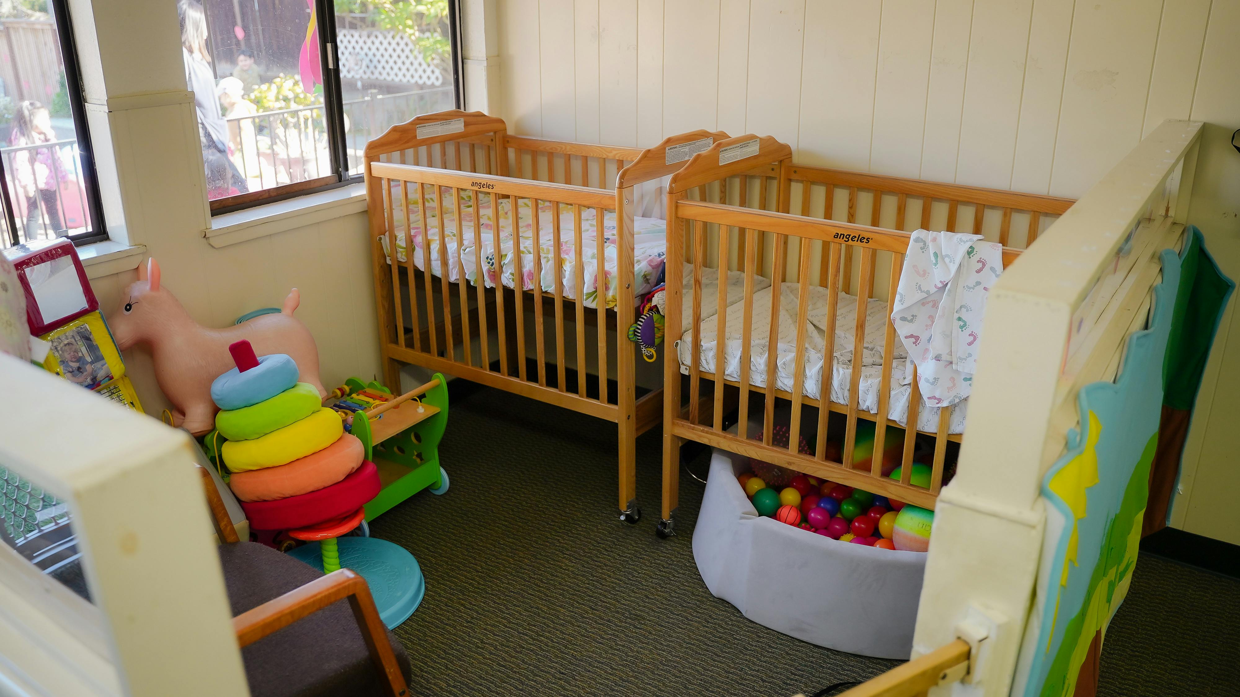 Wooden cribs with toys and a ball pit in a childcare room