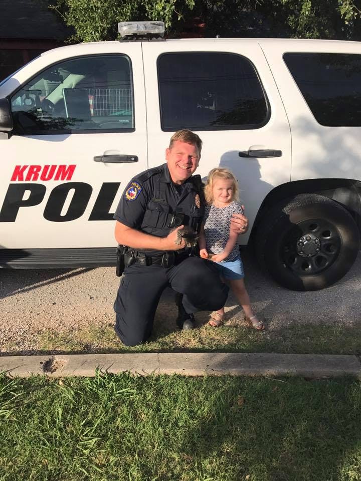 Police officer kneeling next to a child in front of a police vehicle