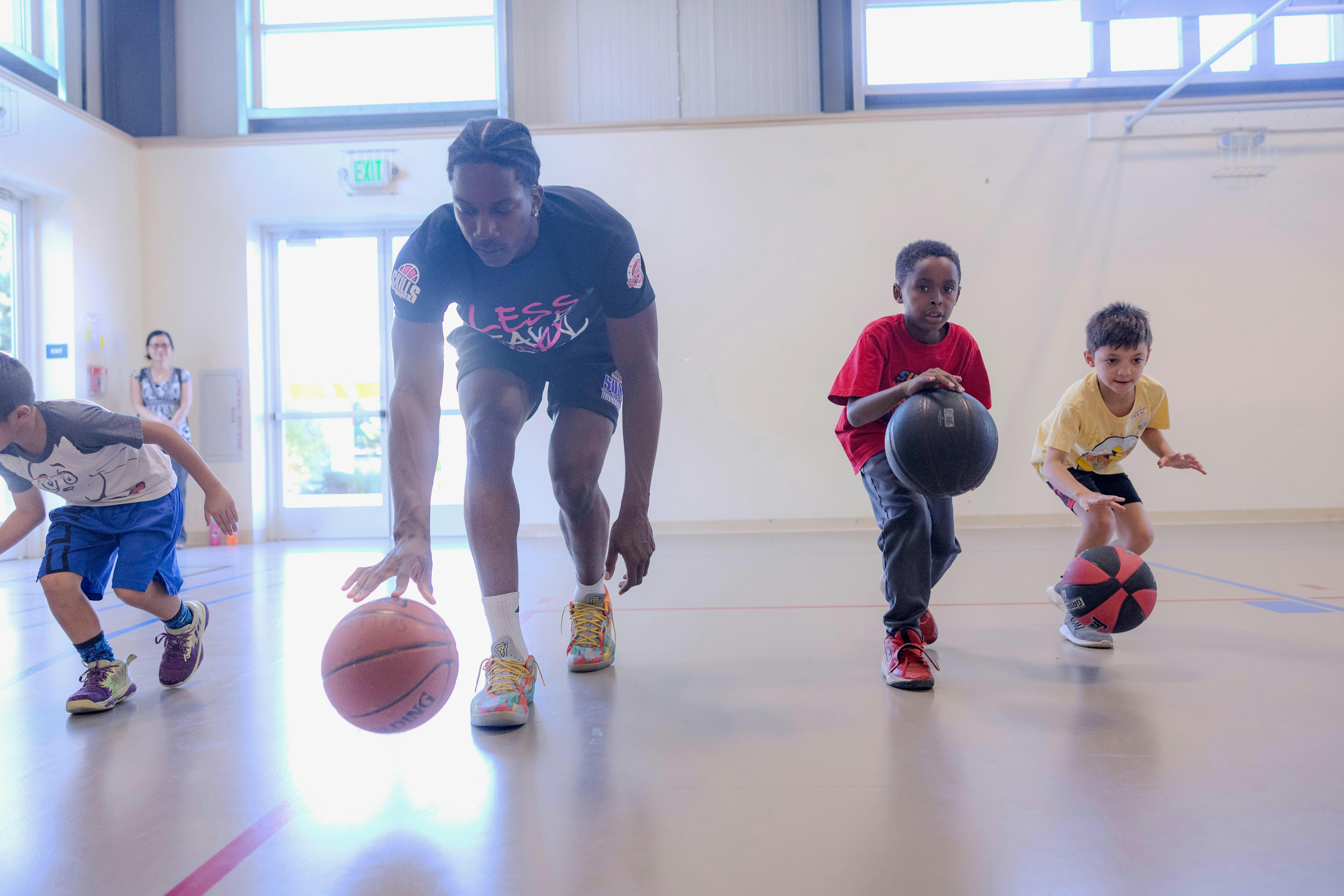 Person and two children dribbling basketballs indoors