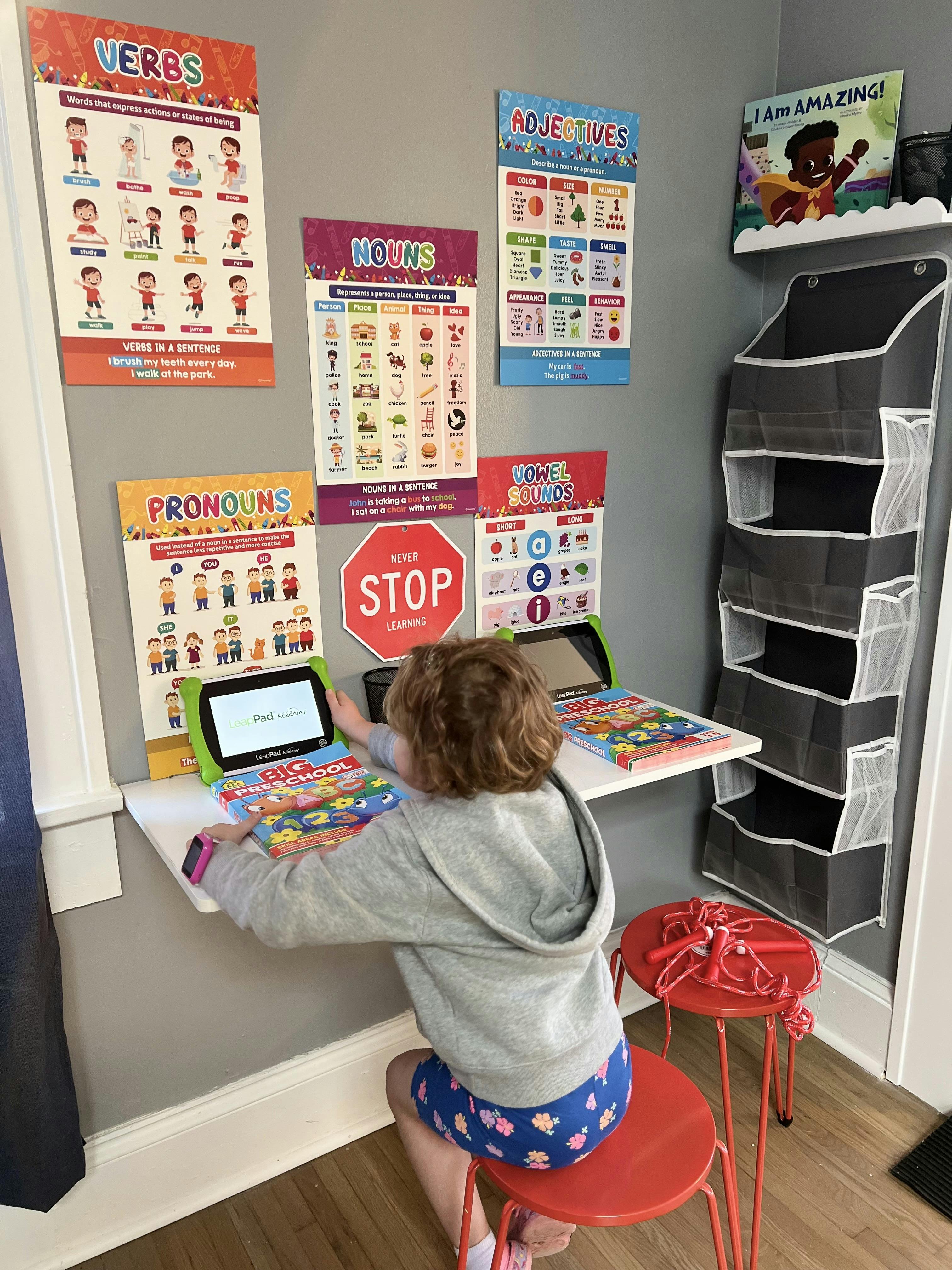 Child sitting at a desk with a tablet and educational posters on the wall
