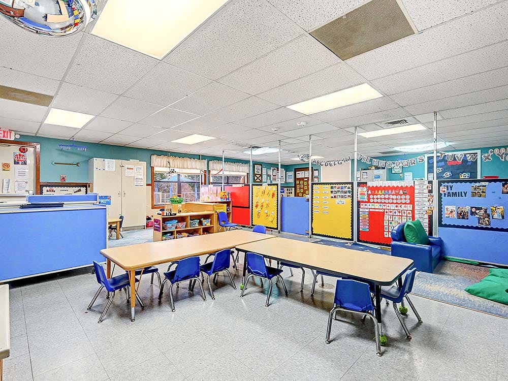 Empty classroom with small tables and chairs, and colorful learning aids on the walls