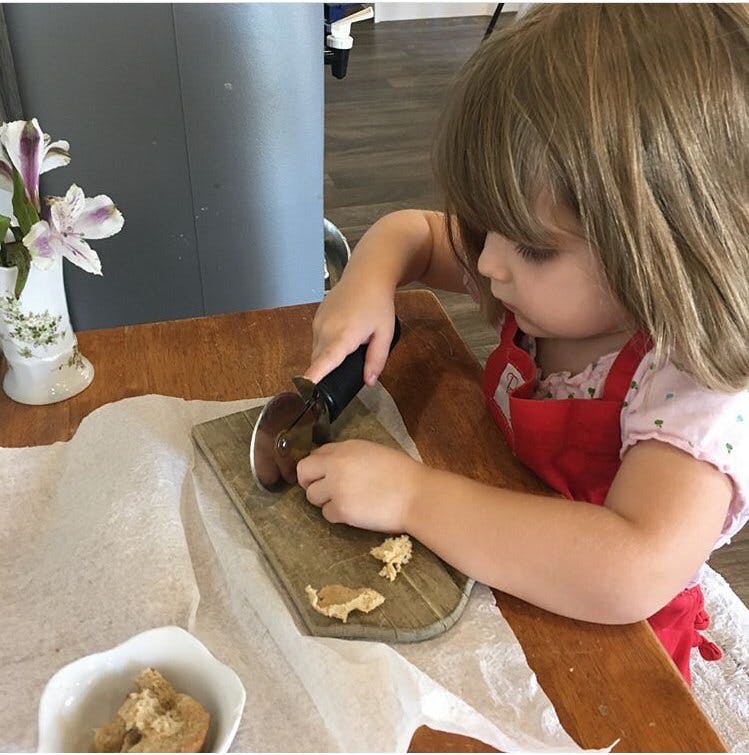 Child using a pizza cutter on dough