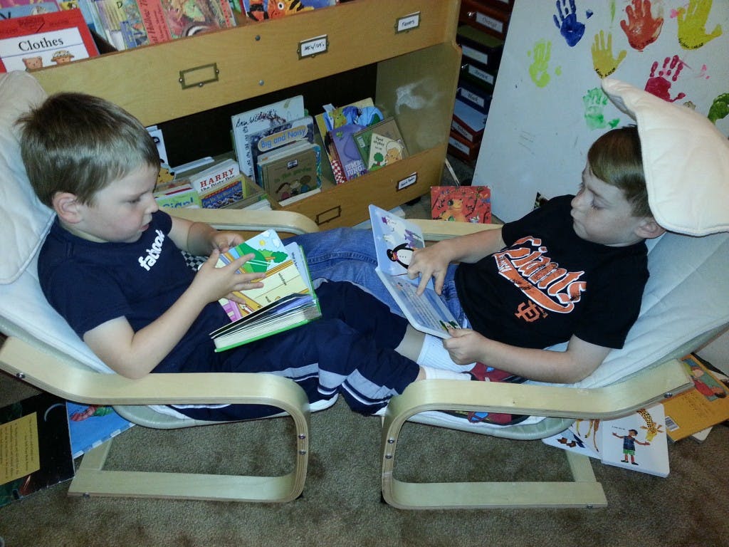 Two children sitting in chairs reading books