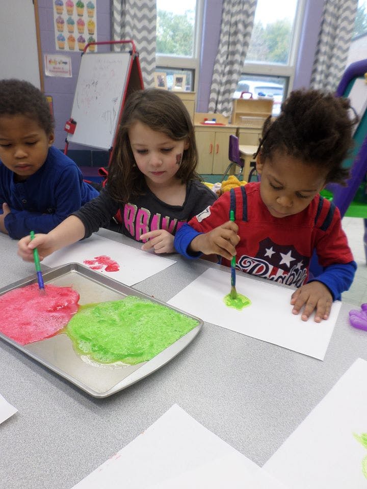 Three children painting with brushes and colorful paint on paper