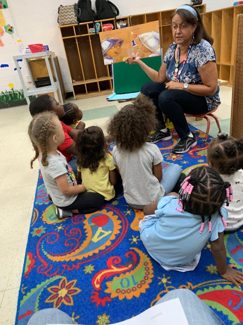 Adult reading a book to a group of children sitting on a rug