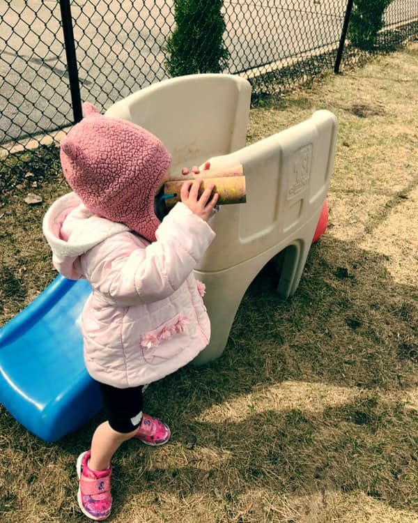 Child drinking from a bottle while standing next to a small slide
