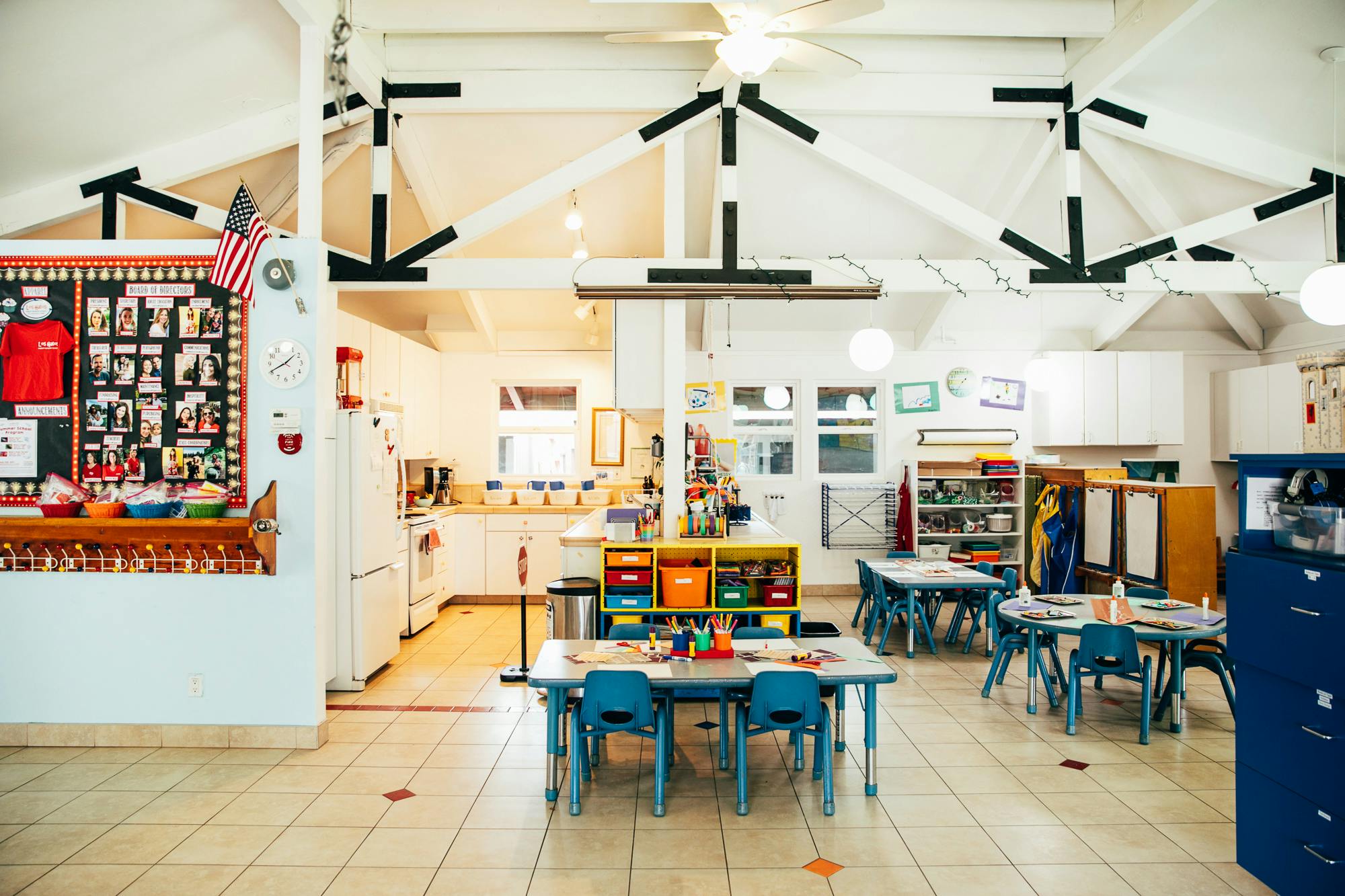 Classroom with small tables and chairs, bulletin board, and kitchen area