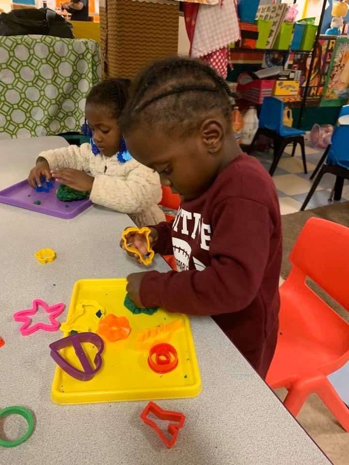 Two children playing with play-doh and cookie cutters at a table