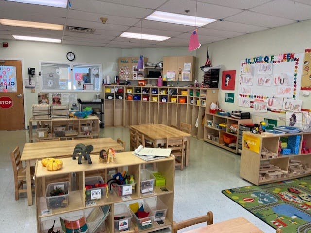 Classroom with tables, chairs, shelving units, and children's artwork on a whiteboard