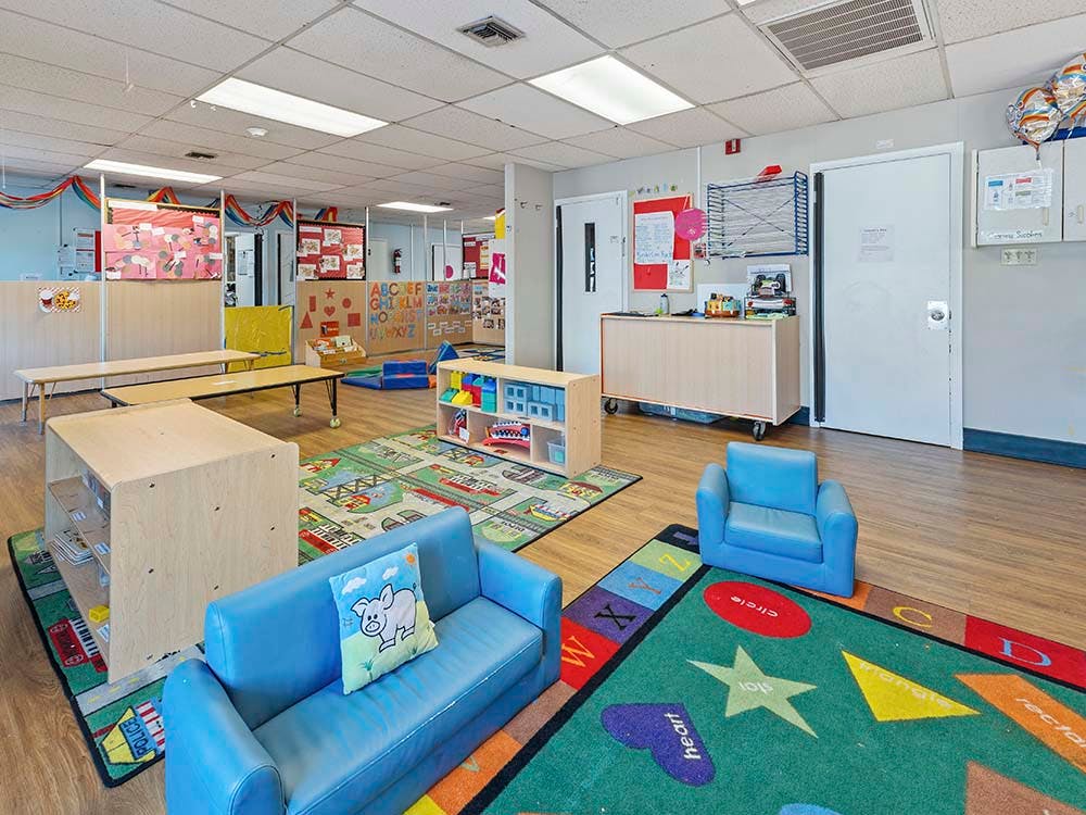 A classroom with small furniture and colorful learning rugs