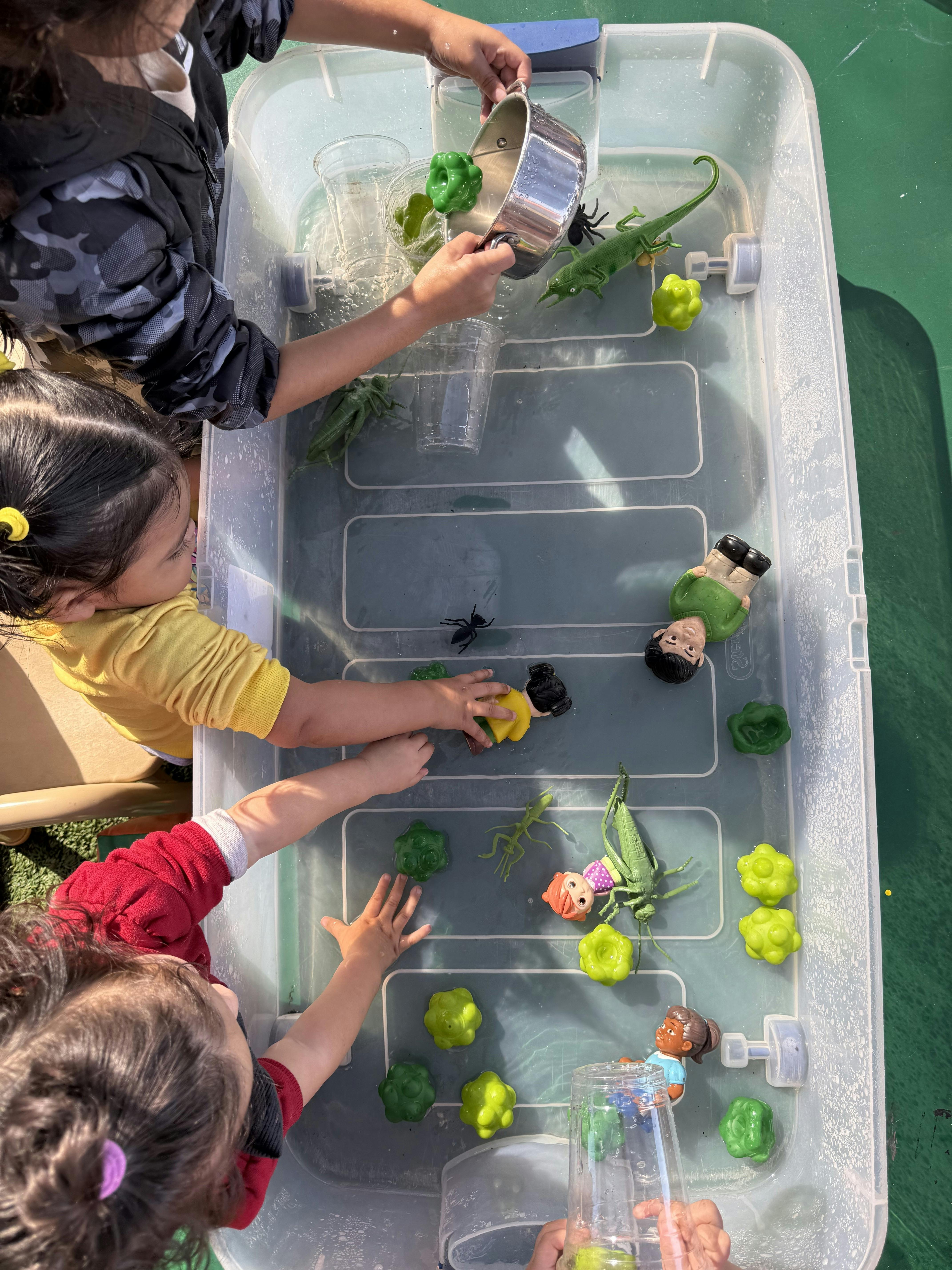 Children playing with toy figures and insects in a water-filled plastic bin