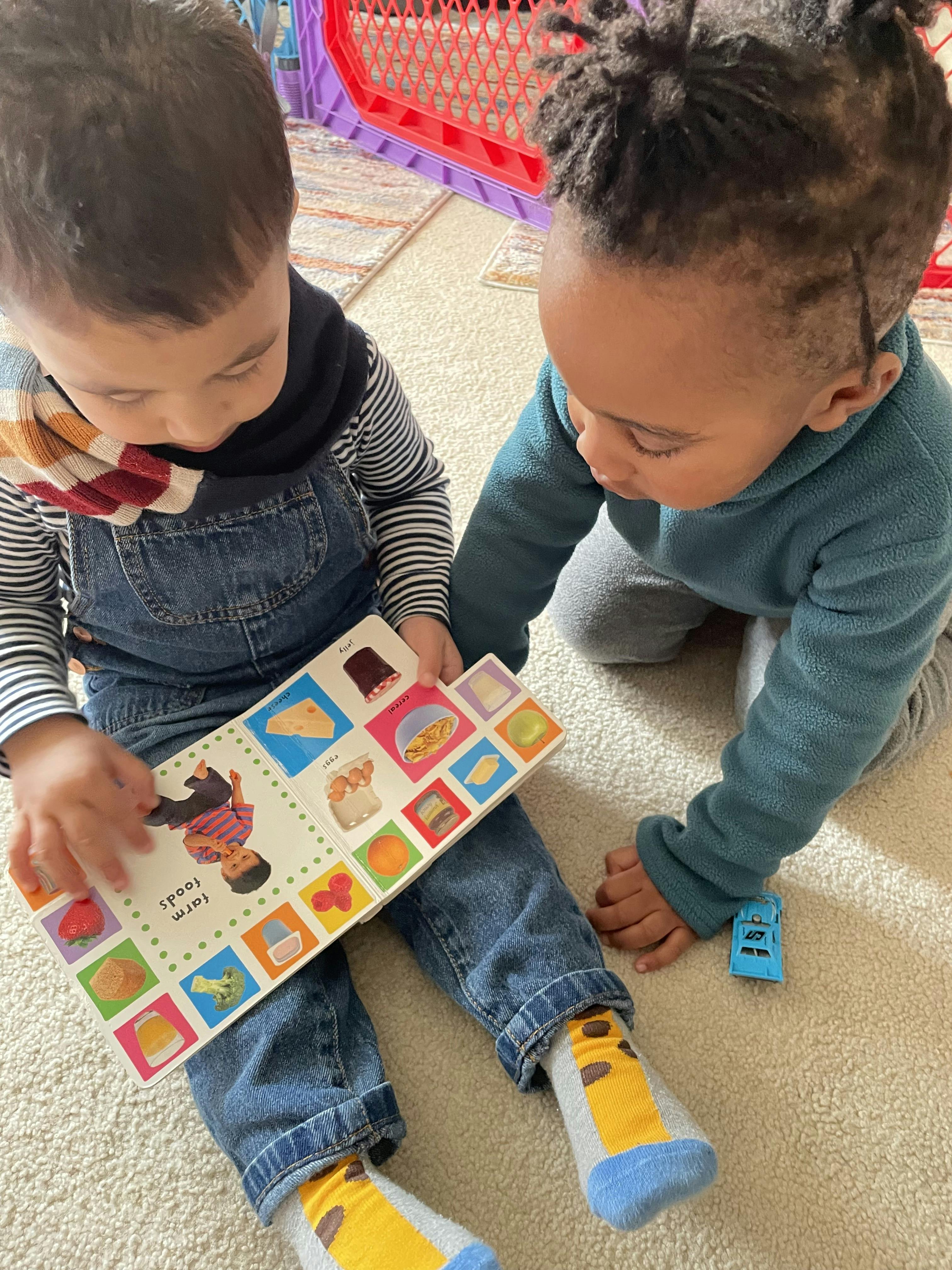 Two children looking at a book and a toy car on the floor