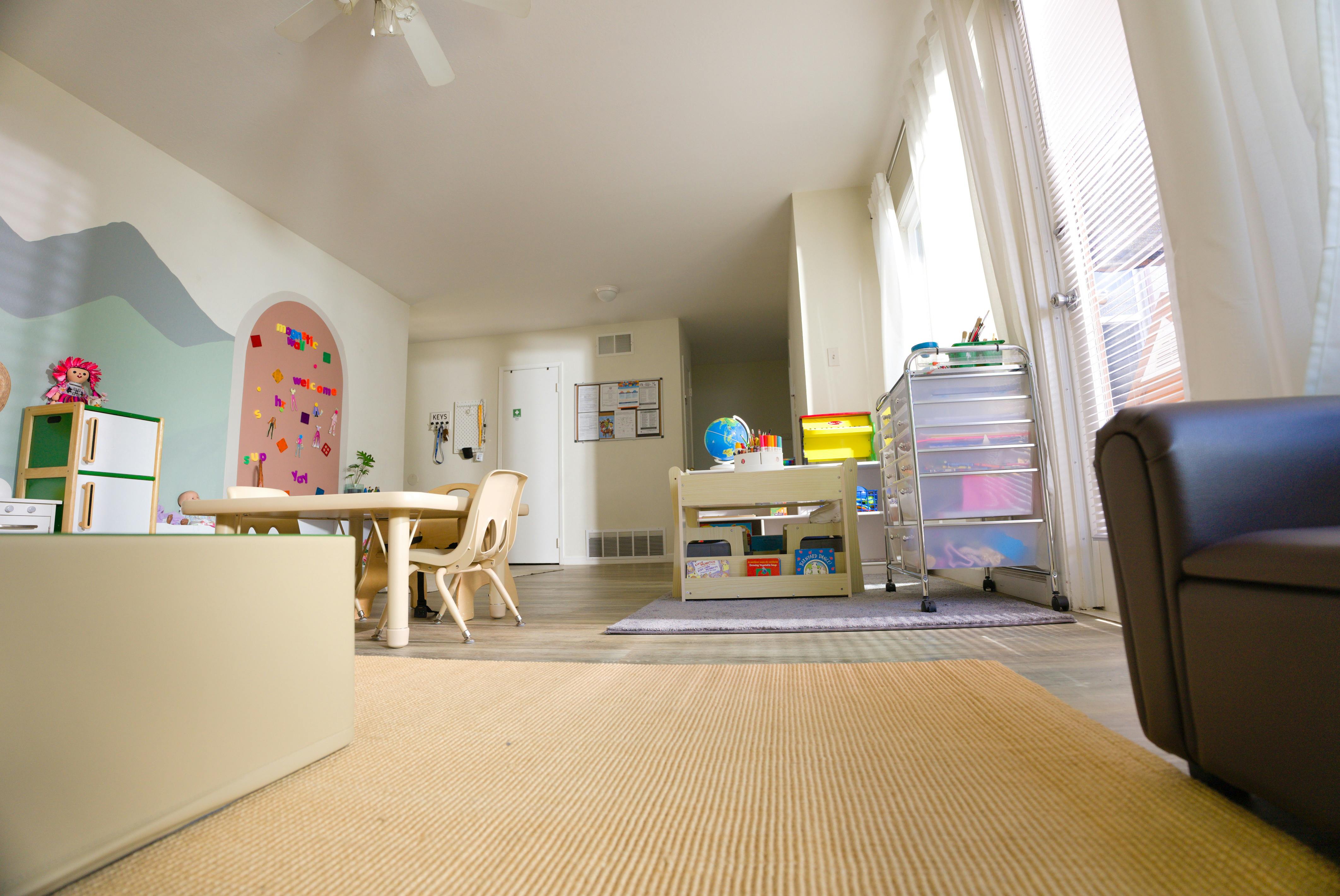A children's playroom with a table, chairs, art supplies, and a magnetic wall