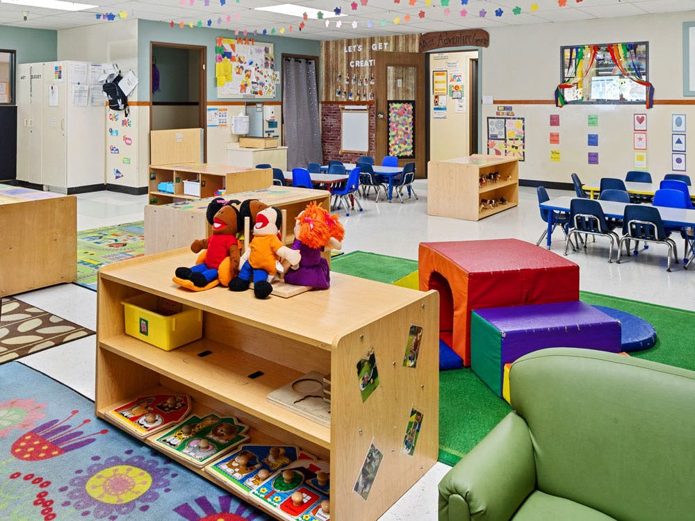 Colorful classroom with tables, chairs, play area, and puppets
