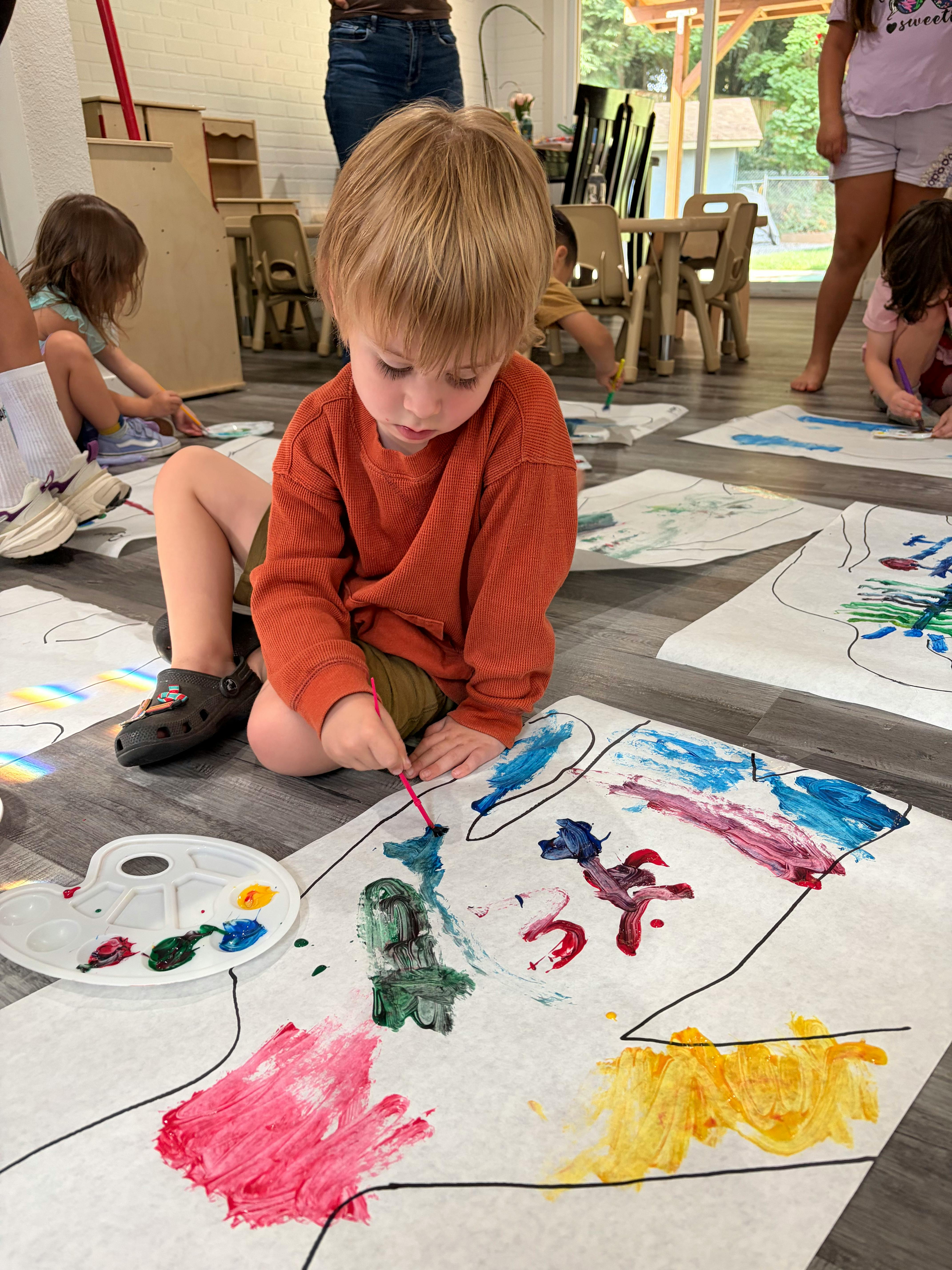 Child painting on large paper sheets on the floor with other children