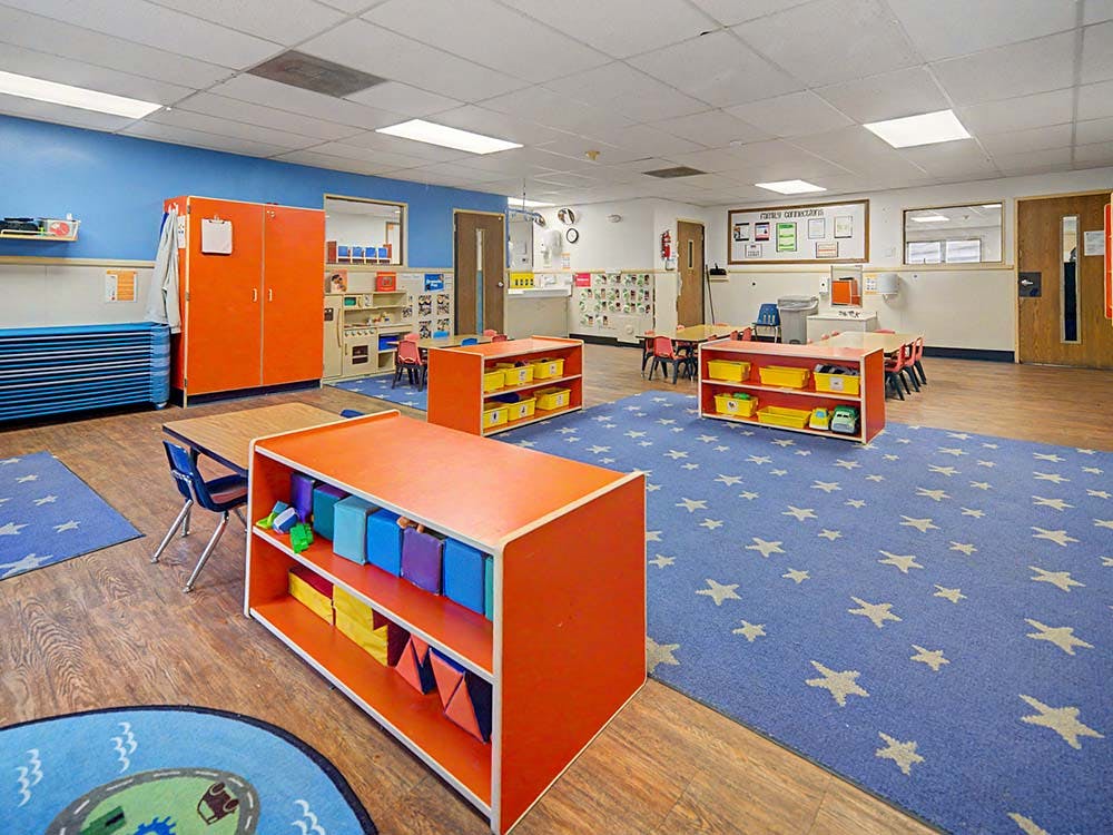Classroom with orange storage shelves, small tables, and blue carpet with stars