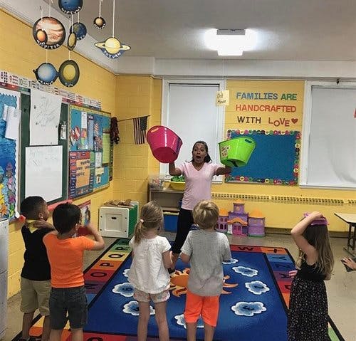 Person holding two buckets in front of children in a classroom