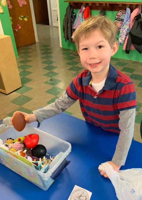 Child holding a toy football over a bin of toys