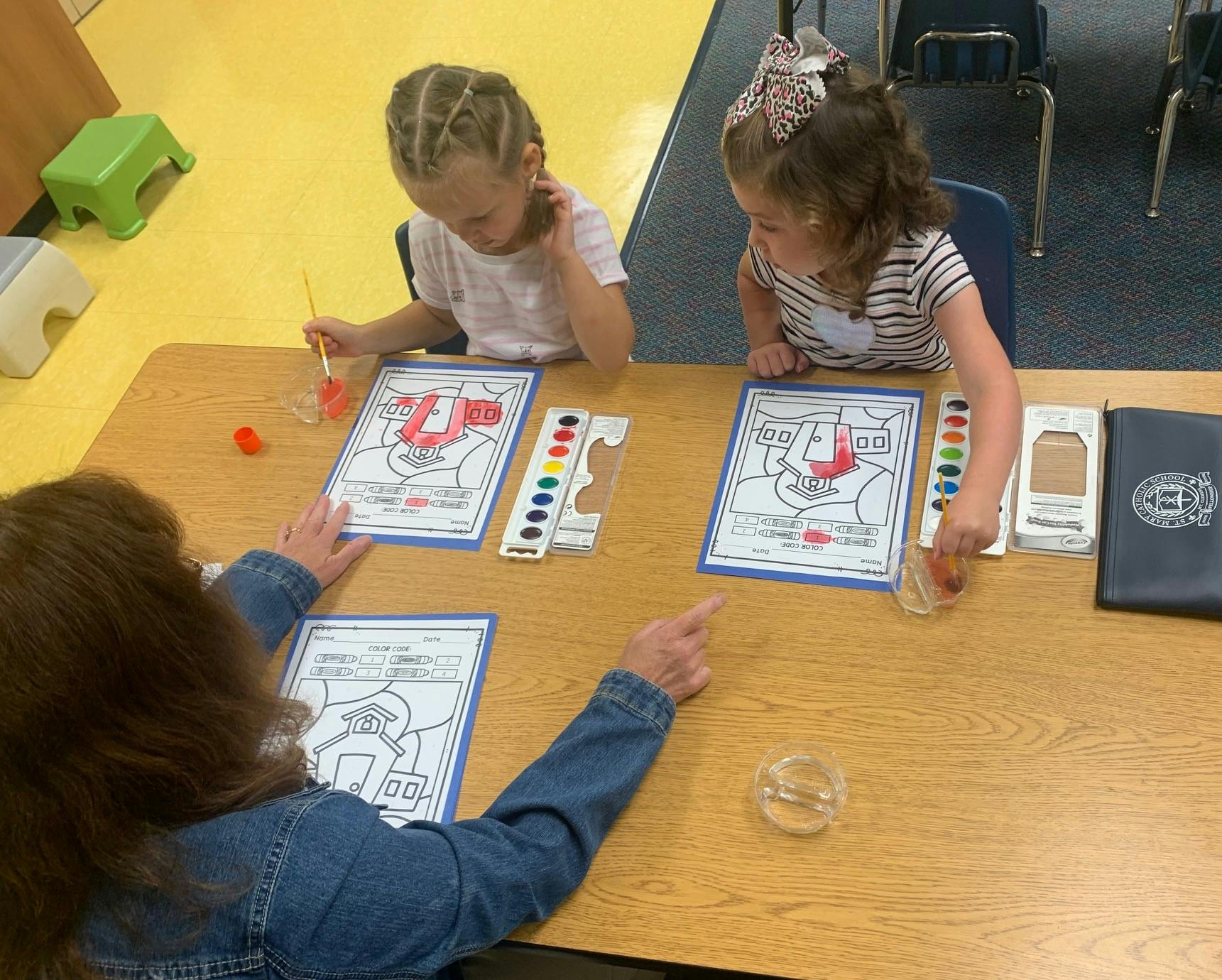 Two children and an adult painting at a table
