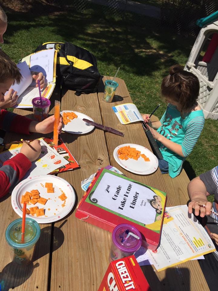 Children eating and doing schoolwork at a picnic table outdoors