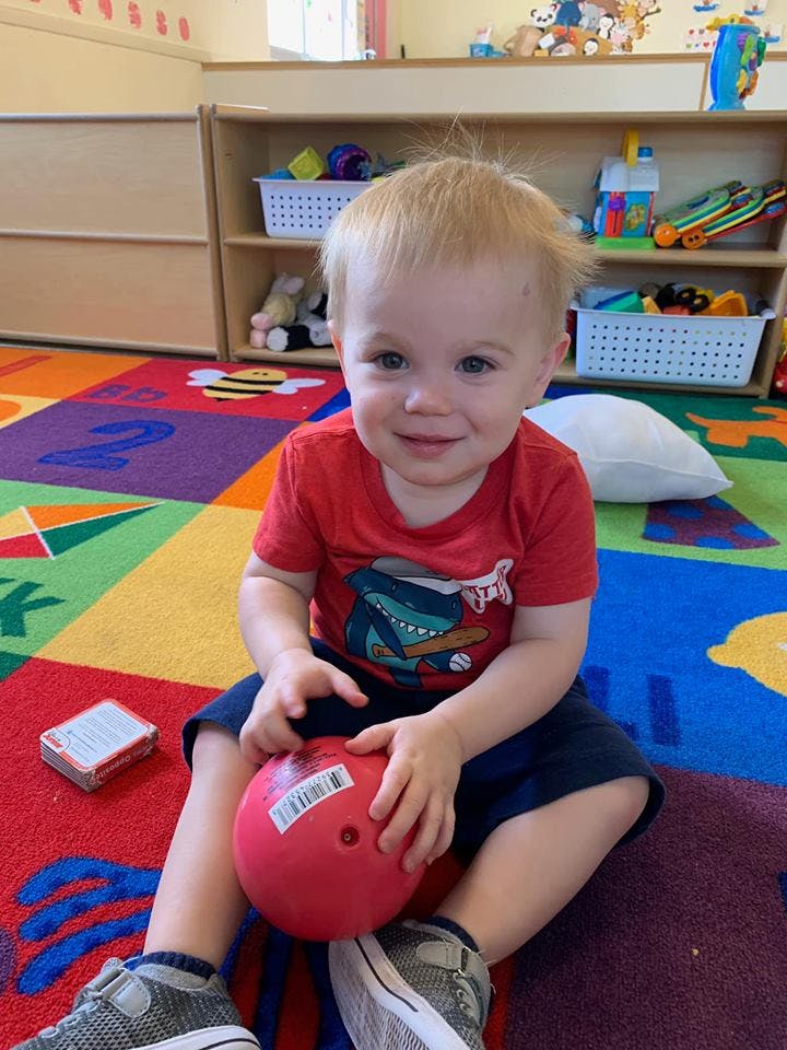 Child sitting on a colorful rug holding a red ball