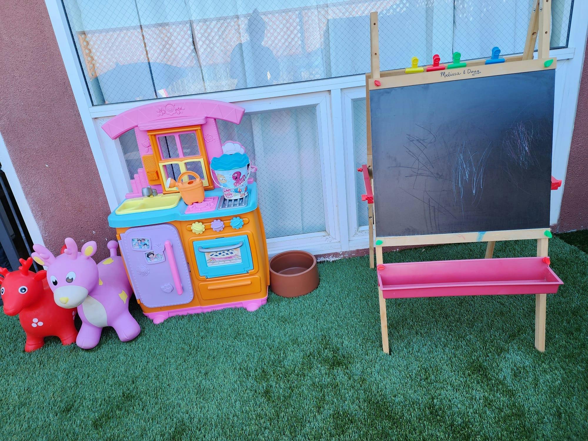 Toy kitchen, two animal hoppers, and a chalkboard easel on artificial grass