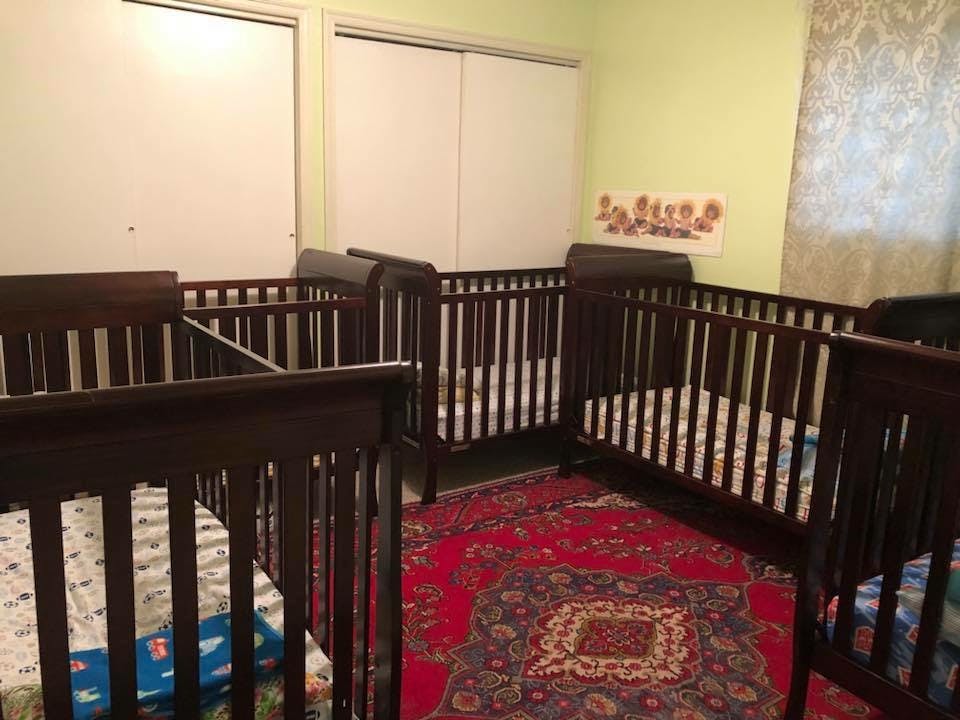 Three wooden cribs in a room with a red patterned rug