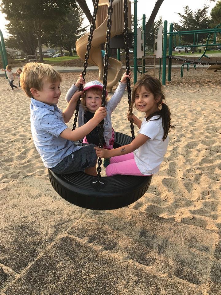 Three children on a tire swing at a playground