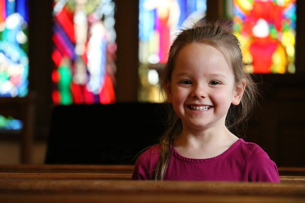 Child smiling in a pew with stained glass windows in the background