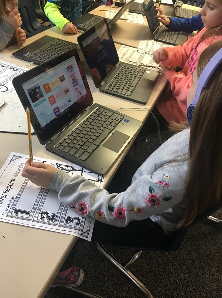 Child writing on paper next to an open laptop