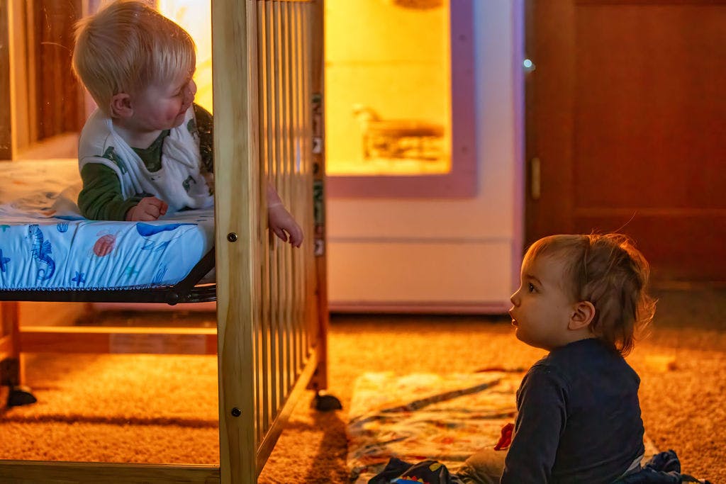 Two children, one in a crib and one on the floor, looking at each other