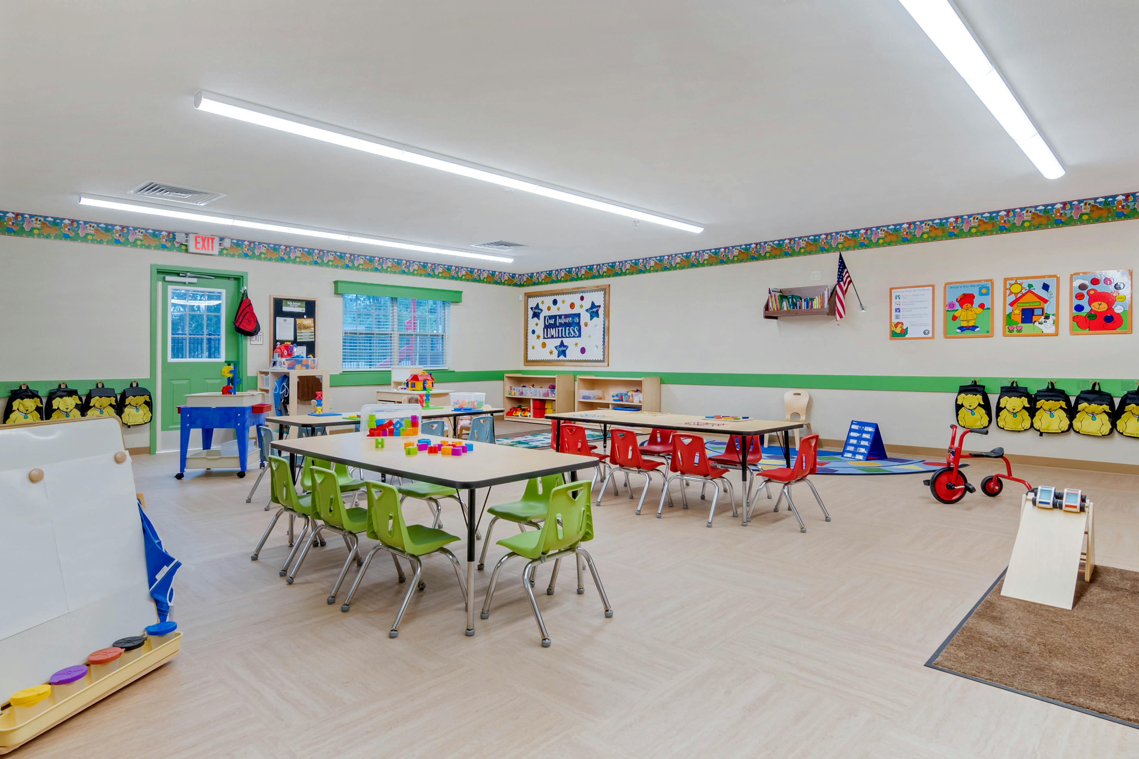 Empty colorful classroom with small tables, chairs, toys, and educational posters