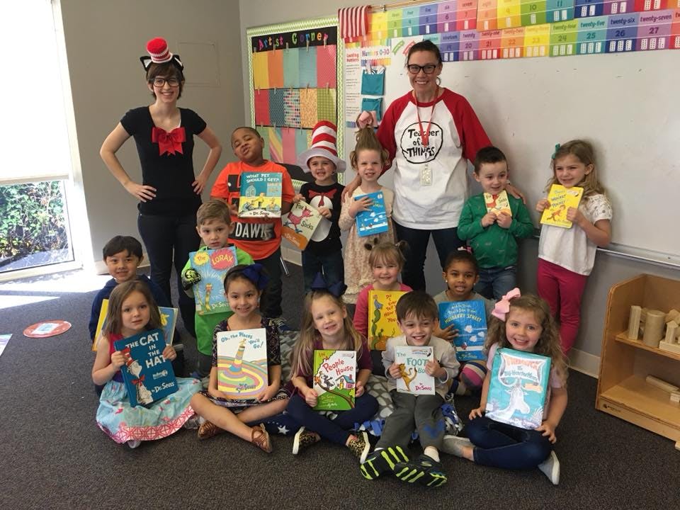 Two adults and multiple children holding books in a classroom