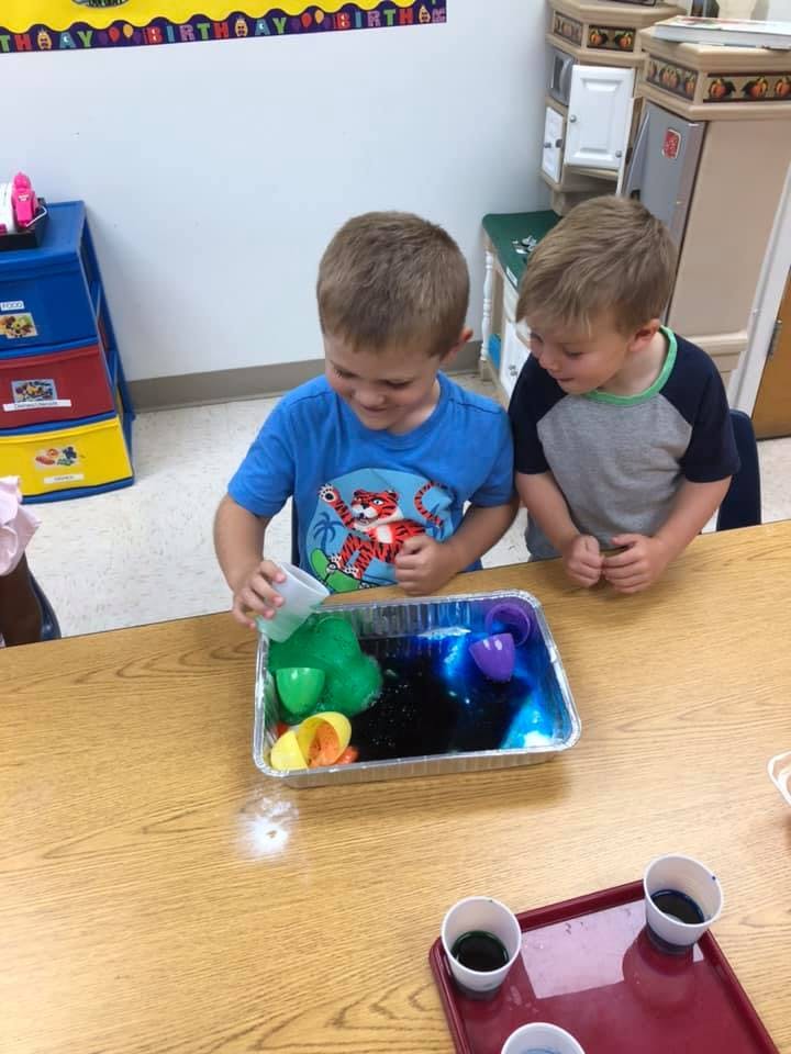 Two children playing with colored water and plastic toys in a classroom