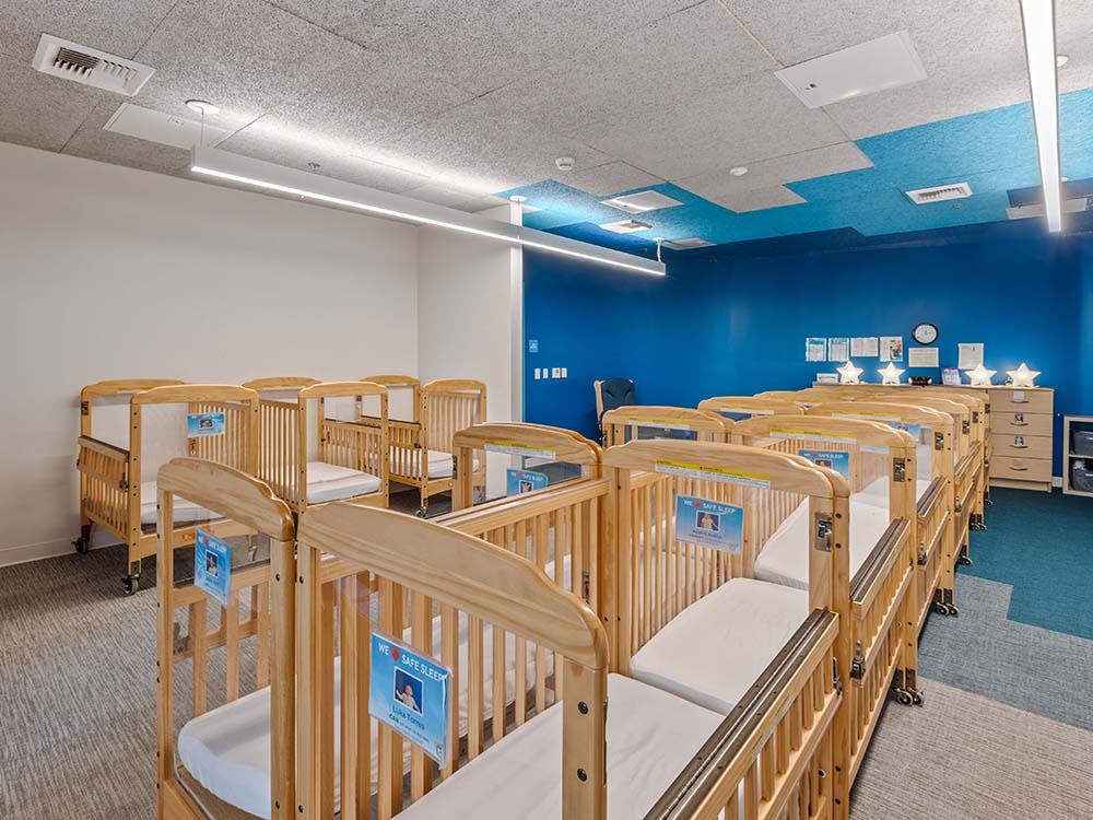 Rows of empty wooden cribs with mattresses in a nursery room