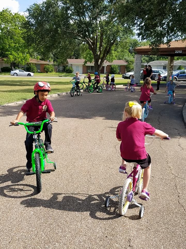 Two children riding bicycles with training wheels on pavement