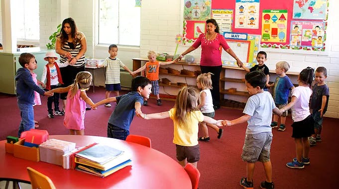 Adults and children holding hands in a circle in a classroom